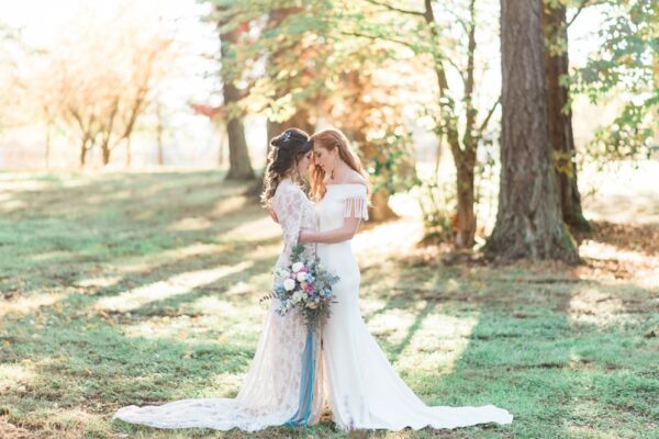 Two women stand in a field dressed in wedding gowns